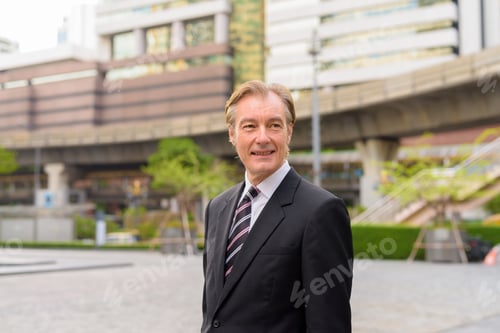 Preview: Happy mature handsome businessman thinking in the city outdoors