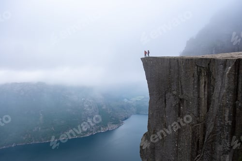 Preview: A panoramic view from the edge of Preikestolen, a cliff in Norway, showcasing two figures standing