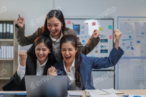 Preview: Three euphoric businesswomen are raising their arms and cheering in front of a laptop, celebrating a