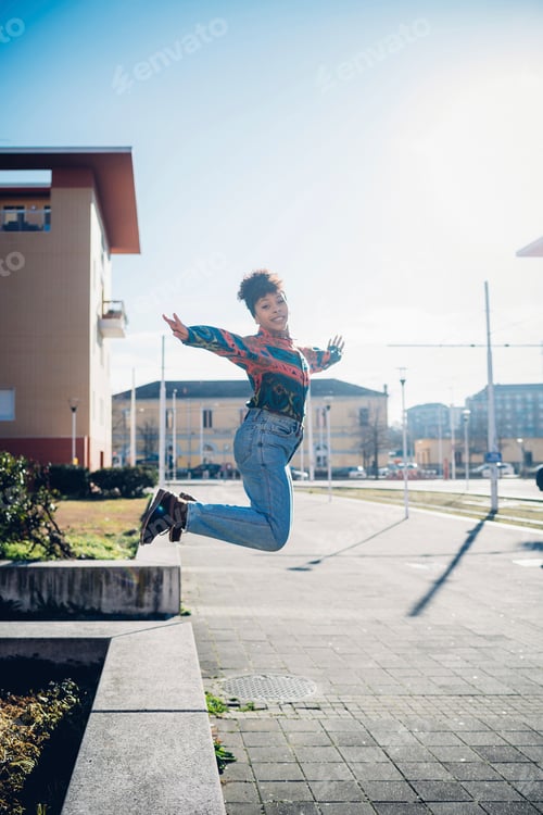 Preview: Young woman jumping from wall on urban sidewalk, full length portrait