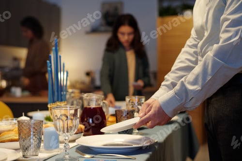 Preview: Close-up of young man putting plates on table served for Hanukkah dinner