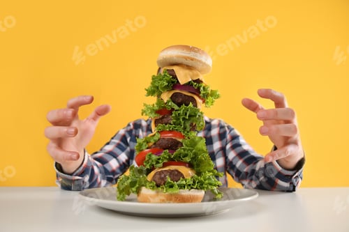 Preview: Hungry man with huge burger at white table on yellow background