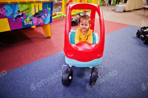 Preview: Cute baby girl rides on a plastic car in indoor play center.