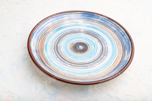 Preview: Empty blue ceramic plate on white concrete background. Side view.