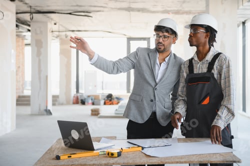 Preview: Architect showing construction plan to builder in building under construction