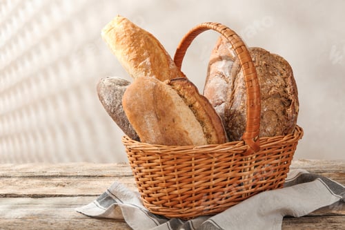 Preview: Different loaves of fresh bread in basket on wooden table, closeup