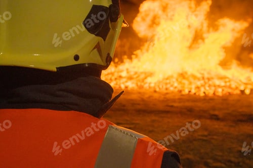 Preview: Firefighter stands before a large fire at night