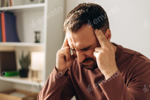 Preview: Stressed Latin businessman holding head, eyes closed, showing pain and exhaustion in office setting