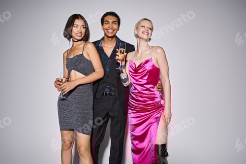 Preview: happy african american man hugging two multiethnic women in dresses with champagne on New Year party