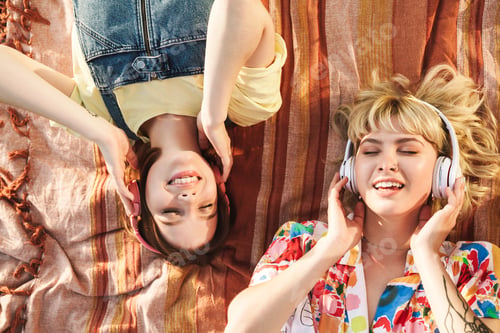 Preview: Image of two women using wireless headphones while lying on blanket