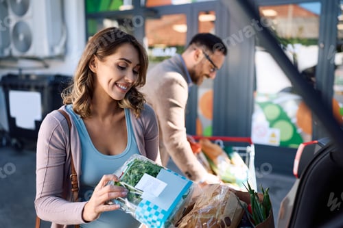 Preview: Happy pregnant woman packing groceries into a car while shopping with her husband.