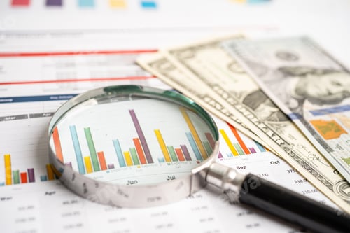 Preview: Magnifying glass on charts graphs paper with US dollar banknotes. Financial development,