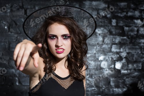 Preview: Young woman dressed as witch pointing to camera.