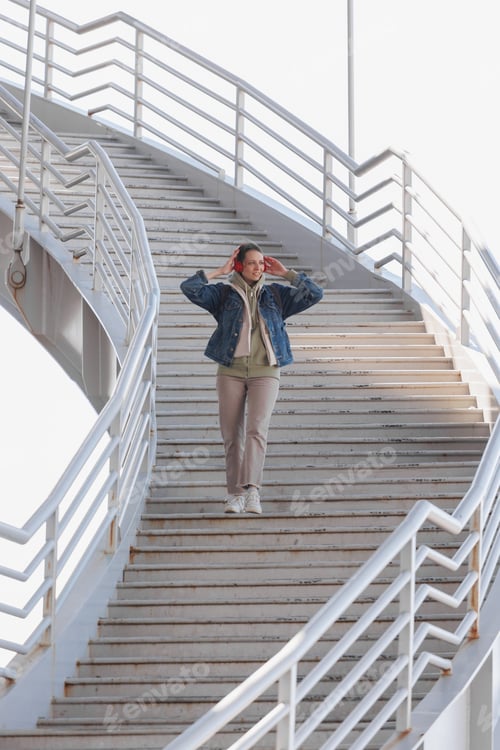 Preview: woman walks up steps and listens to music or podcast with red headphones. full growth