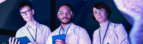 Preview: banner, Three Scientists Examine Newly Created Device in Neon-Lit Science Center