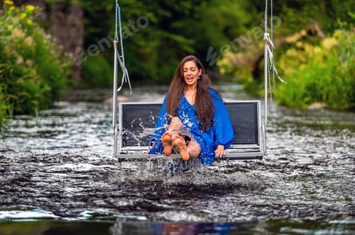 Preview: a joyful young woman swings on a rope swing across a fast-flowing river
