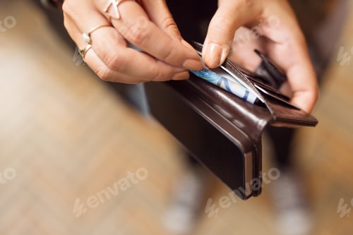 Preview: Woman holding open wallet with banknotes and cell phone