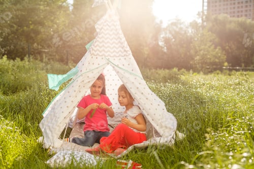 Preview: childhood and hygge concept - happy little girls playing in kids tent