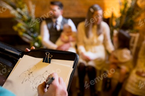 Preview: Over the shoulder view of artist sketching family during naming ceremony in an historic barn.