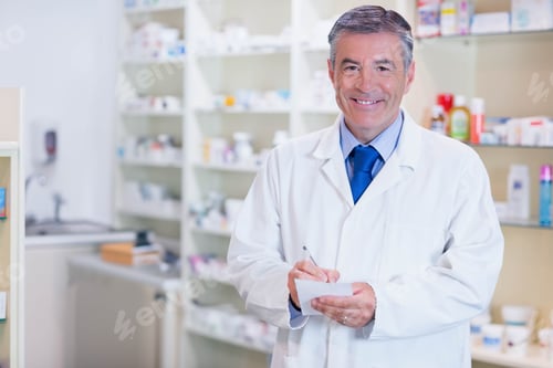 Preview: Middle aged male pharmacist writing on notepad with pen at pharmacy desk with shelves, copy space
