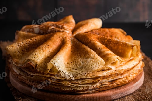 Preview: A stack of thin pancakes on a dark wooden background. A traditional dish of crepes for the holiday