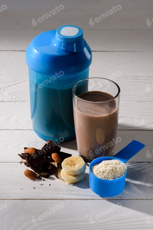 Preview: shaker and glass of protein shake with almond, banana and chocolate on white wooden table