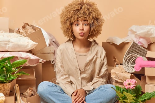 Preview: Lovely woman with curly hair keeps lips folded sends air kiss at camera dressed in shirt and jeans p