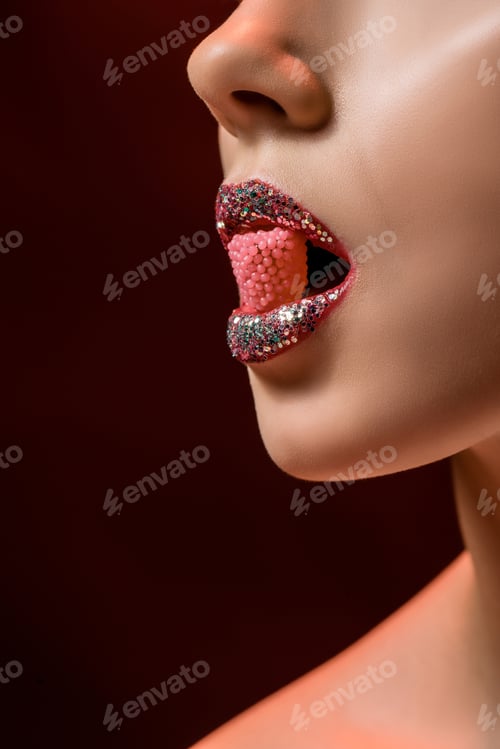 Preview: close up of young woman with shiny lips holding pink candy in mouth on burgundy background