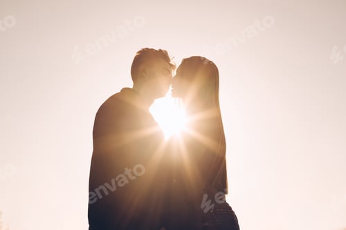 Preview: Couple kissing at sunset with sunbeam in the middle of the two