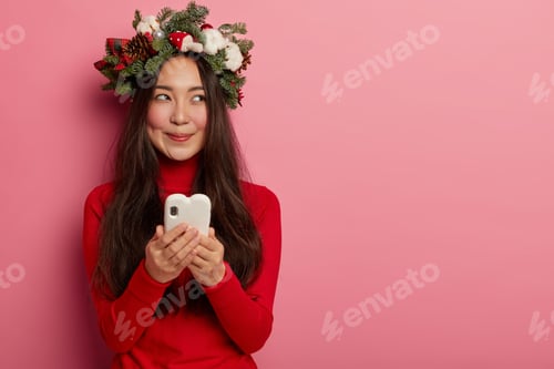 Preview: Dreamy pleasant looking female looks pensively on right side, uses modern cell phone, checks email b