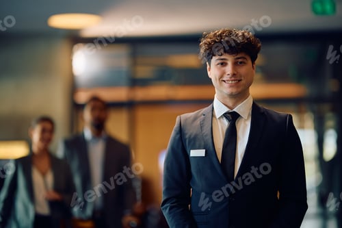 Preview: Happy hotel receptionist standing in a lobby and looking at camera