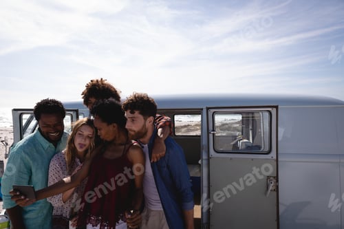 Preview: Group of friends taking a selfie while having beer at beach against a camper van
