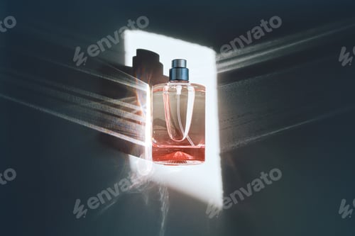 Preview: Pink perfume bottle on the light background in the rays of sun with highlights.