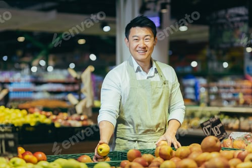 Preview: Portrait of Asian supermarket salesman, man in grocery vegetable section smiling and looking at