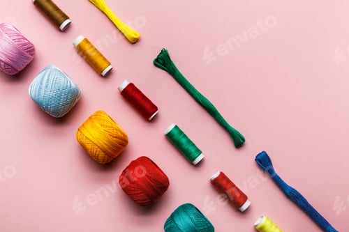 Preview: top view of colorful knitting yarn balls, embroidery threads and thread coils on pink