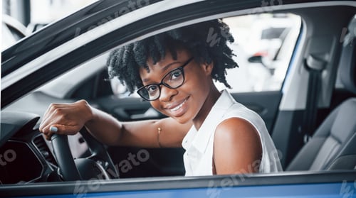 Preview: Cheerful smile. Young african american woman sits inside of new modern car