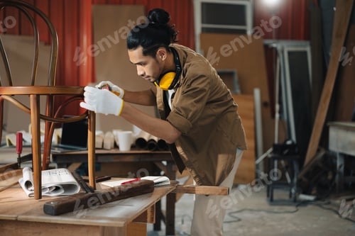 Preview: Young Asian man Carpenter uses a tape measure to measure chair on the workbench
