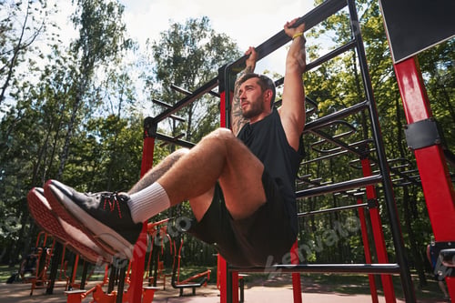 Preview: Young bearded male training abdominal muscles outdoors