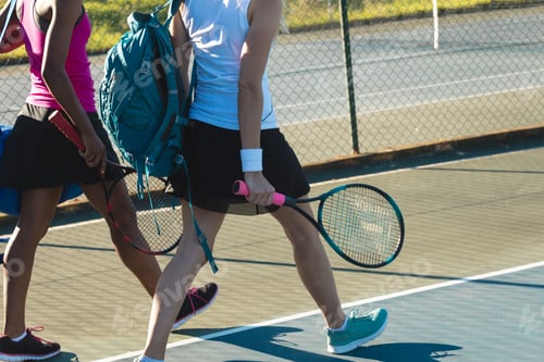 Preview: Low section of multiracial female players walking with backpacks and rackets at tennis court