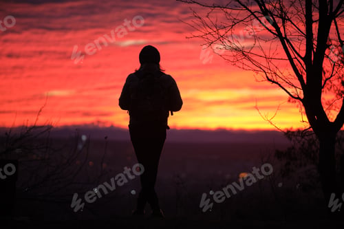 Preview: Dark silhouette of a lonely woman enjoying sunset view in evening nature