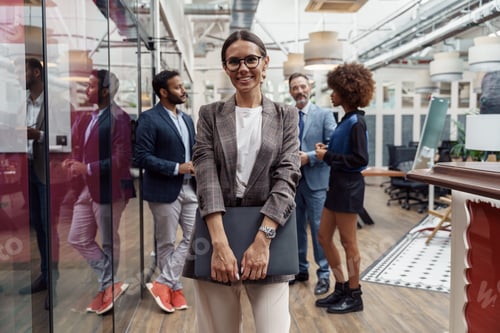 Preview: Portrait of smiling businesswoman in glasses standing in modern office on colleagues background