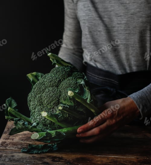 Preview: Crop woman holding fresh broccoli over table