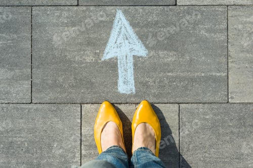 Preview: Female feet with arrow painted on the asphalt.