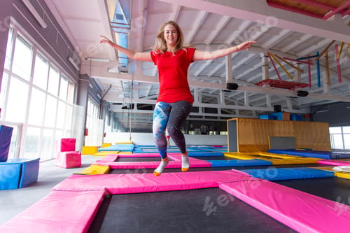 Preview: Fitness, fun, leisure and sport activity concept - Young happy woman jumping on a trampoline indoors
