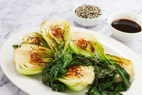Vista previa: Bok choy a la parrilla servido con salsa de soja y semillas de sésamo, en un plato blanco, hecho en casa, sin gente,