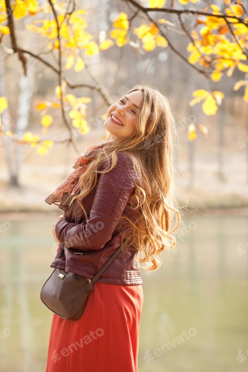 Preview: Beautiful woman in burgundy jacket with long hair in autumn park by the lake smiling and laughing