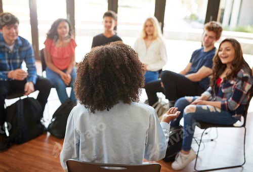 Preview: Rear View Of Female Tutor Leading Discussion Group Amongst High School Pupils