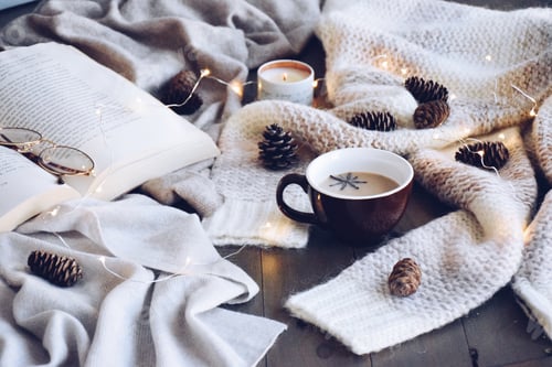 Preview: Cozy sweater, an open book and a warm drink with fairy lights, candle and pine cones