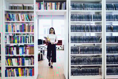 Preview: Female student walking with papers in library