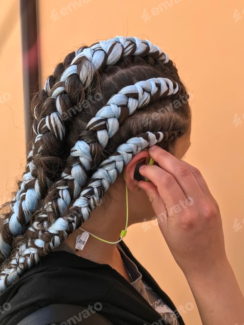 Preview: Girl with blue braids using green wireless headphones / earbuds / earphones. Looking away.
